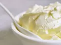 Kremowa masa w białej miseczce z łyżką. Idealna do deserów, gdy szukasz, czym zastąpić mascarpone.