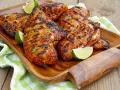 Grillowany kurczak w marynacie, podany z ćwiartkami limonki na drewnianej tacy.