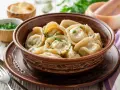 Pielmieni co to? Aromatyczne, gorące pierożki w glinianej misie, posypane zieloną natką. Obok miseczki z masłem i posiekanym szczypiorkiem.