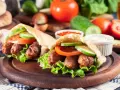 Dwa pyszne **ćevapi** w bułce z sałatą, pomidorem i ogórkiem, podane z sosem.