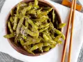 Miseczka pełna błyszczącej, przyprawionej fasolki edamame, posypanej sezamem. Obok leżą pałeczki do jedzenia.