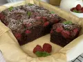 Czekoladowe ciasto z malinami, posypane cukrem pudrem i udekorowane listkami mięty. Idealne na deser.