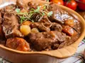 Gęsta, aromatyczna łata wołowa z warzywami i grzybami, podana w glinianej misie, udekorowana gałązką ziół.