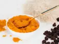Miseczka pełna intensywnej przyprawy curry, obok ryż i rodzynki. Złota łyżeczka zanurzona w aromatycznym proszku.