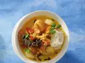 Aromatyczna zupa krewetkowa z krewetkami, makaronem ryżowym, papryczką chili i kolendrą, podana w białej misce na niebieskim tle.