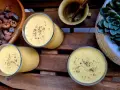 Trzy szklanki kremowego mango lassi, posypane przyprawami, obok miski z suszonymi owocami i sukulentu.