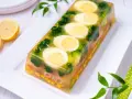 Eleganckie jajka w galarecie z brokułami i kukurydzą, ozdobione plasterkami cytryny.