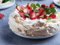 Puszysty tort bezowy z mascarpone i bitą śmietaną, ozdobiony świeżymi truskawkami i miętą.