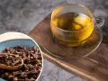 Napar z goździków przepis: aromatyczna herbata w szklance i miseczka pełna goździków na drewnianej desce.