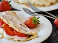 Słodki omlet z truskawkami i bitą śmietaną, posypany cukrem pudrem. Idealny przepis na omlet na słodko.
