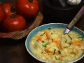 Aksamitna zupa kalafiorowa z makaronem, ozdobiona natką pietruszki. Obok miski leżą świeże pomidory.