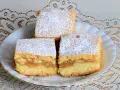 Trzy kawałki ekspresowego ciasta z jabłkami, posypane cukrem pudrem, na białym talerzu z koronkowym obrusem.