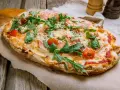 Pinsa co to? Podłużna, chrupiąca pizza z rukolą, pomidorkami i szynką parmeńską, posypana parmezanem.