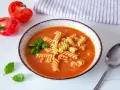 Aksamitna zupa pomidorowa z makaronem fusilli, ozdobiona bazylią. Idealne jakie przyprawy do zupy pomidorowej? Świeże pomidory obok sugerują prostotę i smak.