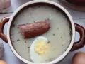 Aromaticzny żurek z kiełbasą i jajkiem, przygotowany na bazie domowego zakwasu na żurek. Obok czosnek, cebula i jajka.