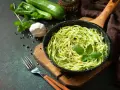 Pyszny makaron keto z cukinii w patelni, udekorowany bazylią. Obok czosnek, pieprz i świeże cukinie.