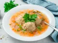Szybka zupa na obiad z klopsikami, ryżem i warzywami, udekorowana natką pietruszki.