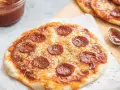 Pyszna pizza z tortilli na patelni, z serem i pepperoni, gotowa do podania. Obok sos i łyżeczka.