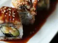 Rolka sushi z wężem morskim, polana słodkim sosem unagi i posypana sezamem, leży na talerzu.