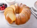 Pyszna babka piaskowa, przepis sprawdzony, posypana cukrem pudrem, obok miseczka z owocami leśnymi i widelce.