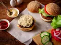 Pyszny sos do burgera, ketchup i majonez czekają na idealne kanapki. Obok świeże warzywa i bułki z sezamem.