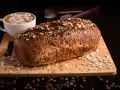 Pyszny chleb keto z twarogu i jajek, posypany płatkami owsianymi i czarnuszką, obok kawy z pianką w kształcie misia.