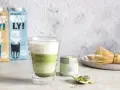 Zielony napój warstwowy w szklance, obok puszka z napisem "PREMIUM MATCHA" i bambusowa miotełka. To jest właśnie co to matcha.