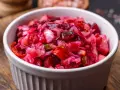 Prosta sałatka z buraków gotowanych, z dodatkiem cebuli i ogórka kiszonego, podana w białej miseczce.