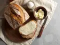 Chleb na drożdżach przepis: świeżo upieczony bochenek, kromka z masłem, miseczka masła i sól. Idealny na śniadanie.