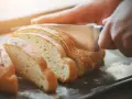 Dłoń kroi świeży chleb na kromki. Zastanawiasz się, jak odświeżyć chleb? Ten obrazek pokazuje, jak zacząć.