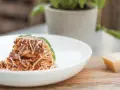 Pyszne spaghetti bolognese, przygotowane według oryginalnego przepisu, posypane parmezanem i udekorowane listkiem bazylii.