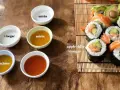 Zastanawiasz się, czym zastąpić ocet ryżowy? Na stole widzisz miseczki z octem, mirinem, sokiem z cytryny i sosami, a obok sushi.