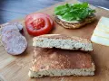 Kromka chleba keto, plasterki kiełbasy, pomidor i ser na desce. Idealne składniki na keto kanapkę.