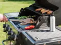 Ręka szczypcami obraca na grillu pyszny halloumi z grilla, obok pieką się papryczki i pomidory.