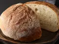 Chleb na drewnianej desce, jeden bochenek przekrojony, ukazujący puszysty miąższ. Idealny przepis na chleb naszych babć.