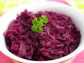 Miseczka pełna aromatycznej, czerwonej kapusty na ciepło, udekorowana gałązką natki pietruszki. Idealny dodatek do obiadu.
