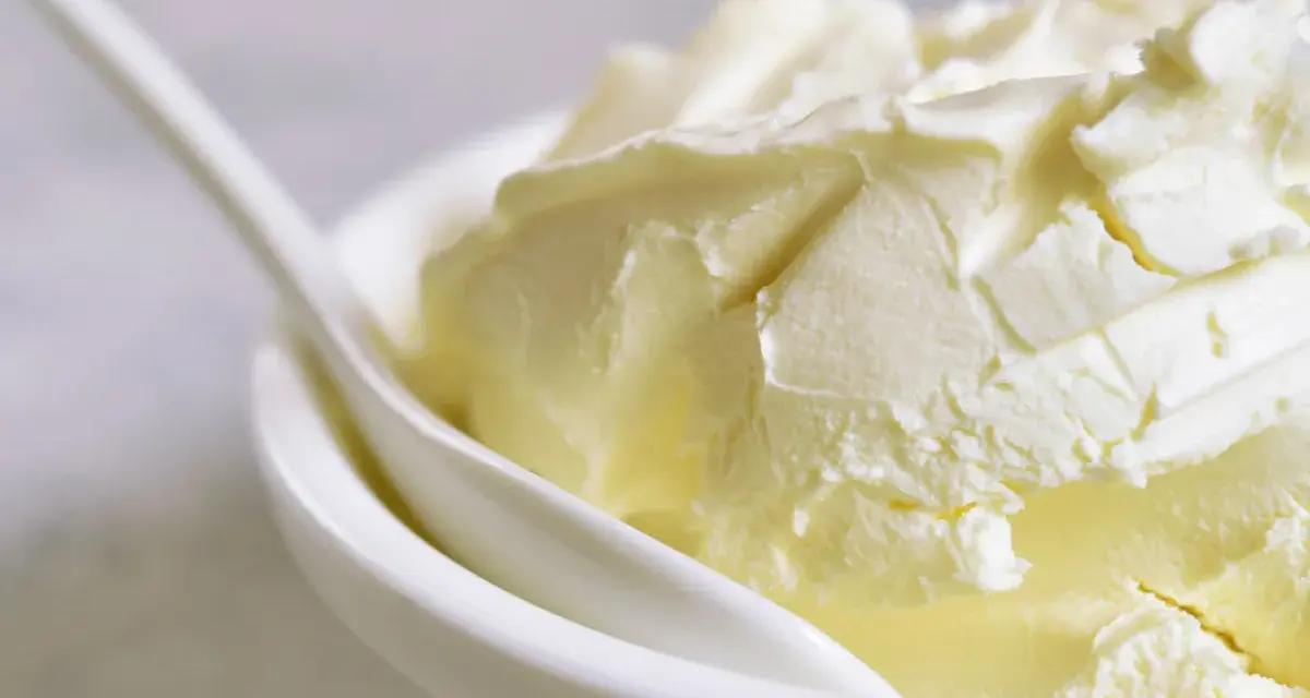 Kremowa masa w białej miseczce z łyżką. Idealna do deserów, gdy szukasz, czym zastąpić mascarpone.