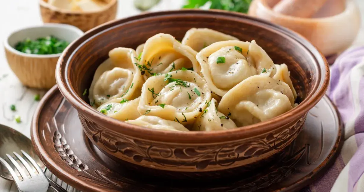 Pielmieni co to? Aromatyczne, gorące pierożki w glinianej misie, posypane zieloną natką. Obok miseczki z masłem i posiekanym szczypiorkiem.
