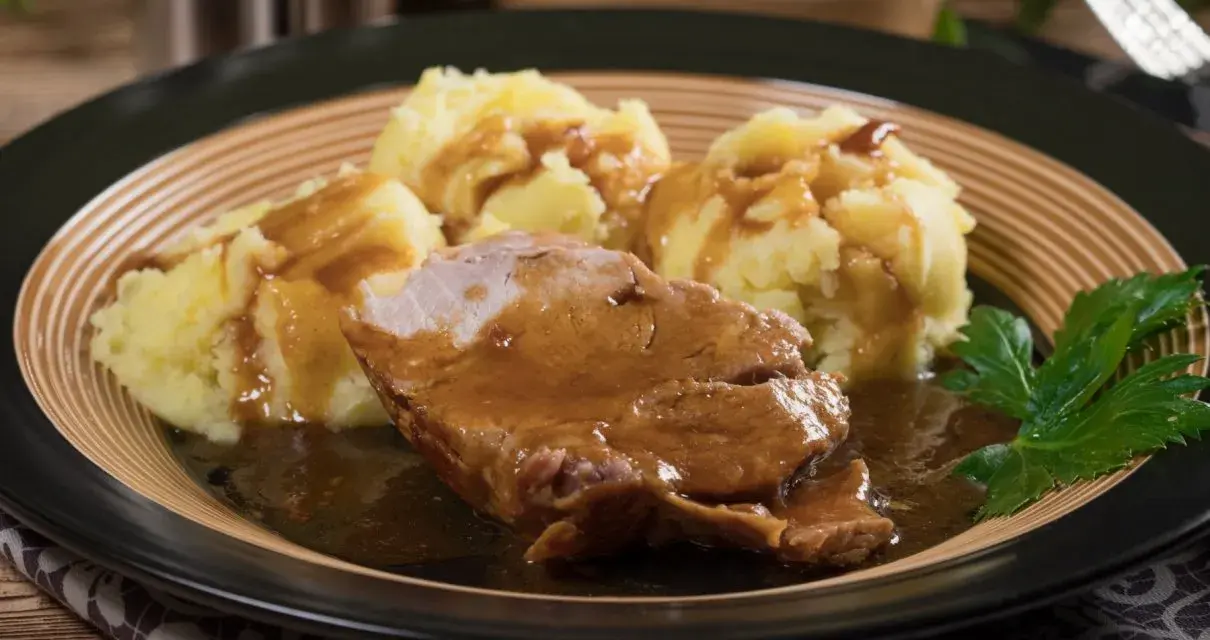 Karkówka w sosie własnym z purée ziemniaczanym, udekorowana natką pietruszki. Pyszny sos do karkówki idealnie komponuje się z ziemniakami.