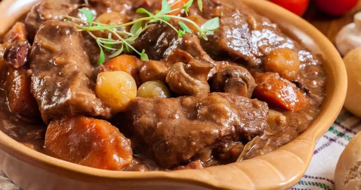 Gęsta, aromatyczna łata wołowa z warzywami i grzybami, podana w glinianej misie, udekorowana gałązką ziół.