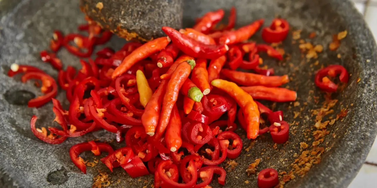 Ostry jak diabli! Całe mnóstwo czerwonych papryczek chili, niektóre pokrojone w plasterki, leżą w kamiennym moździerzu. To zapowiada najostrzejszą paprykę!