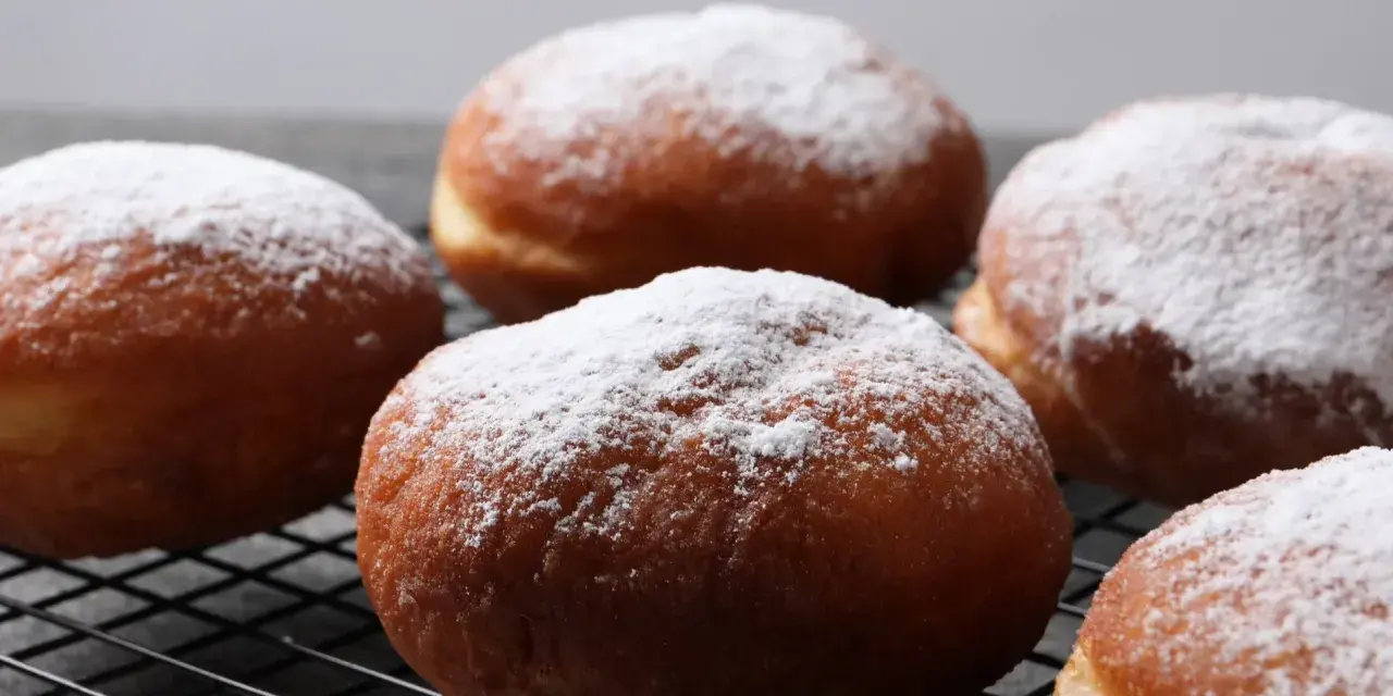 Szybkie pączki z piekarnika, oprószone cukrem pudrem, wyglądają apetycznie na czarnej kratce.