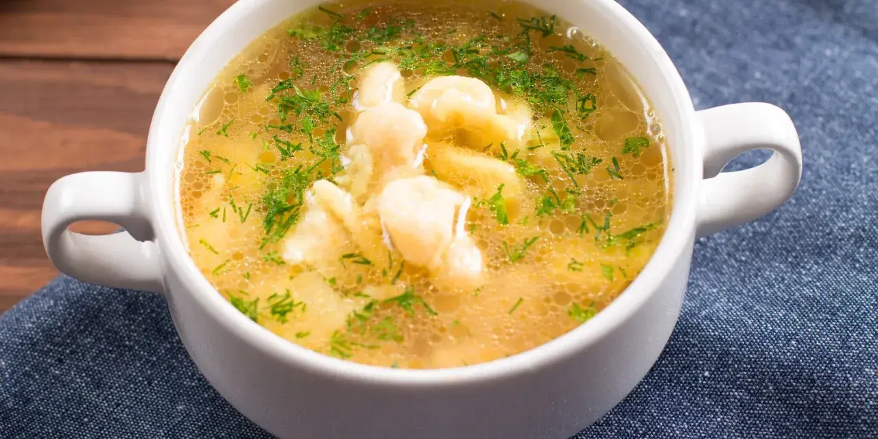 Aromaticzna zupa zacierkowa z koperkiem, podana w białej miseczce na granatowym obrusie.