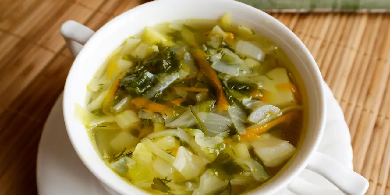 Aromaticzna zupa z młodej kapusty z ziemniakami i marchewką, podana w białej miseczce na bambusowej macie.