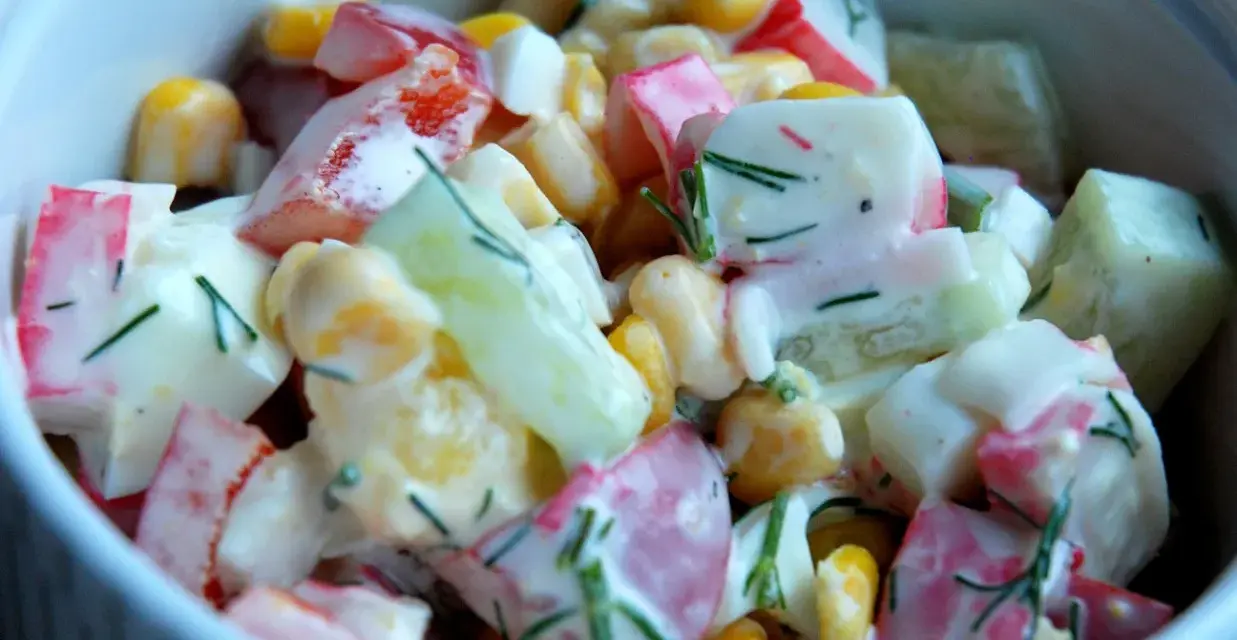 Pyszna, kremowa sałatka z surimi, kukurydzą, ogórkiem i jajkiem, posypana świeżym koperkiem. Idealna na każdą okazję, to najlepsza sałatka z surimi!