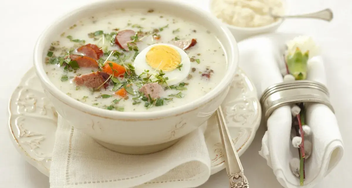 Aromaticzny żurek z białą kiełbasą i jajkiem, podany w misce, z dodatkiem ziół i marchewki. Idealny prosty przepis na żurek.