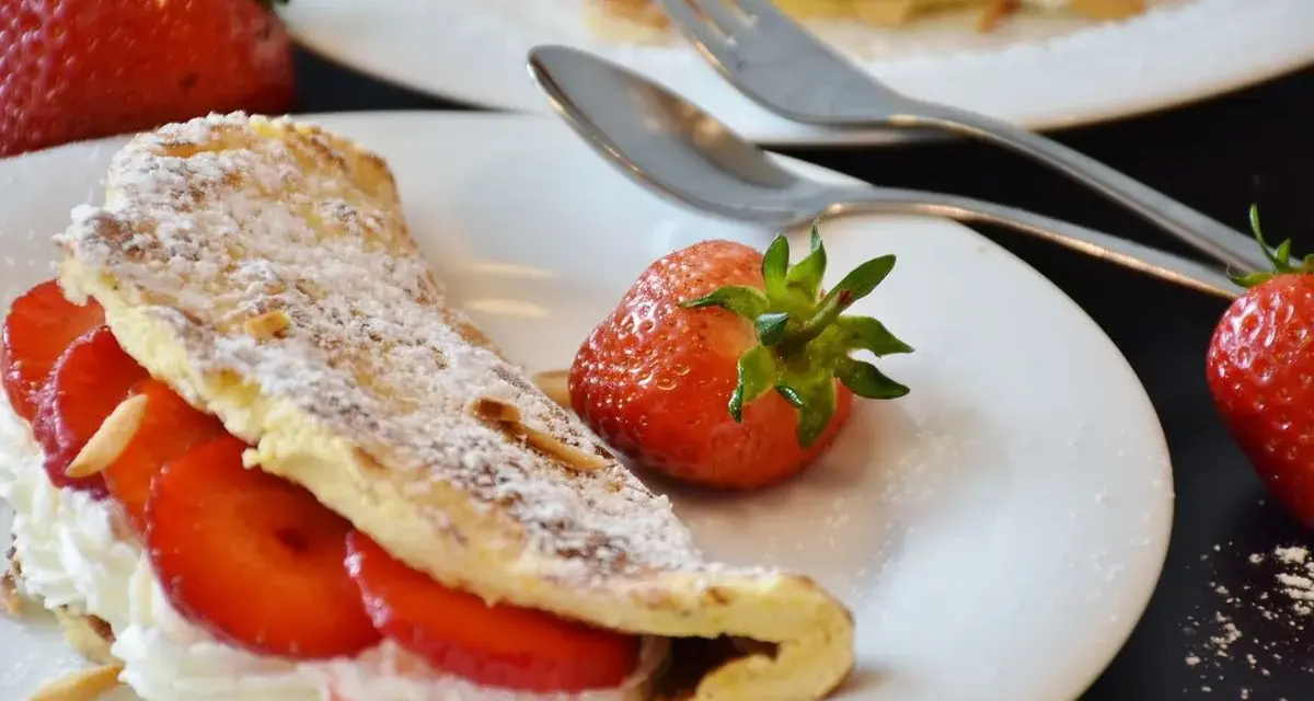 Słodki omlet z truskawkami i bitą śmietaną, posypany cukrem pudrem. Idealny przepis na omlet na słodko.