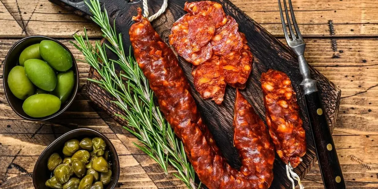Chorizo co to? Pikantna, wędzona kiełbasa na desce z oliwkami, kaparami i rozmarynem. Idealna przekąska.