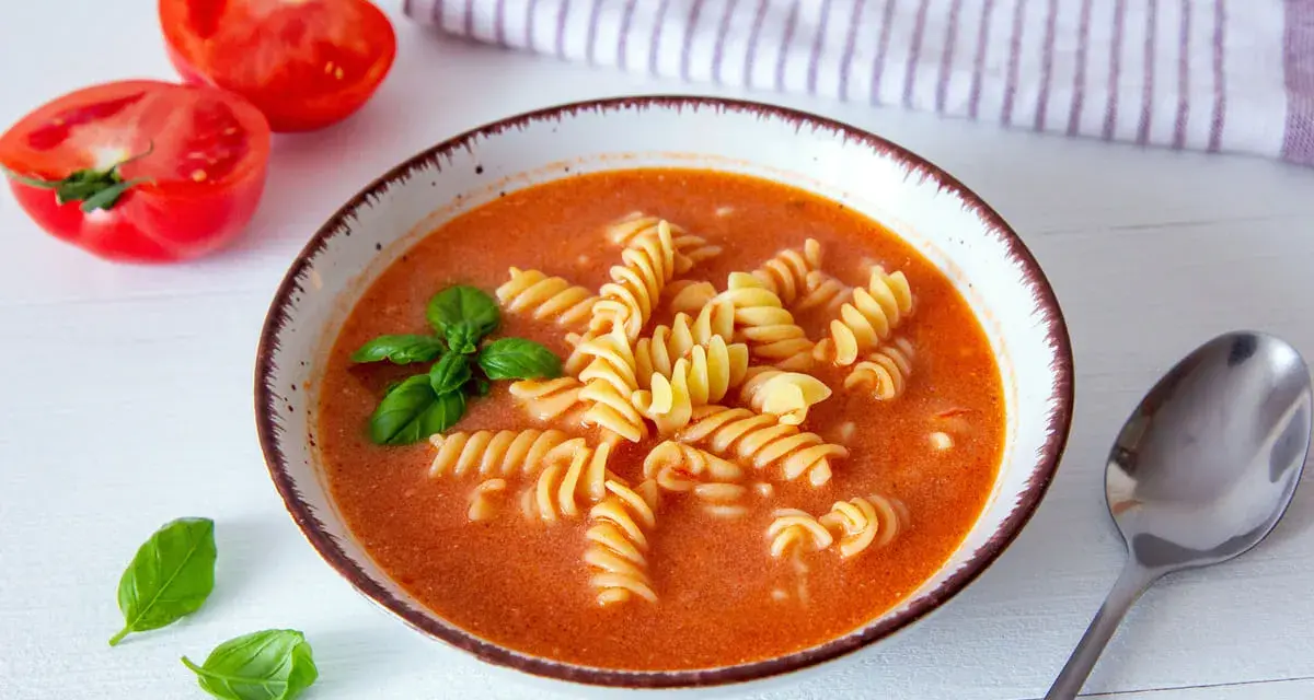 Aksamitna zupa pomidorowa z makaronem fusilli, ozdobiona bazylią. Idealne jakie przyprawy do zupy pomidorowej? Świeże pomidory obok sugerują prostotę i smak.