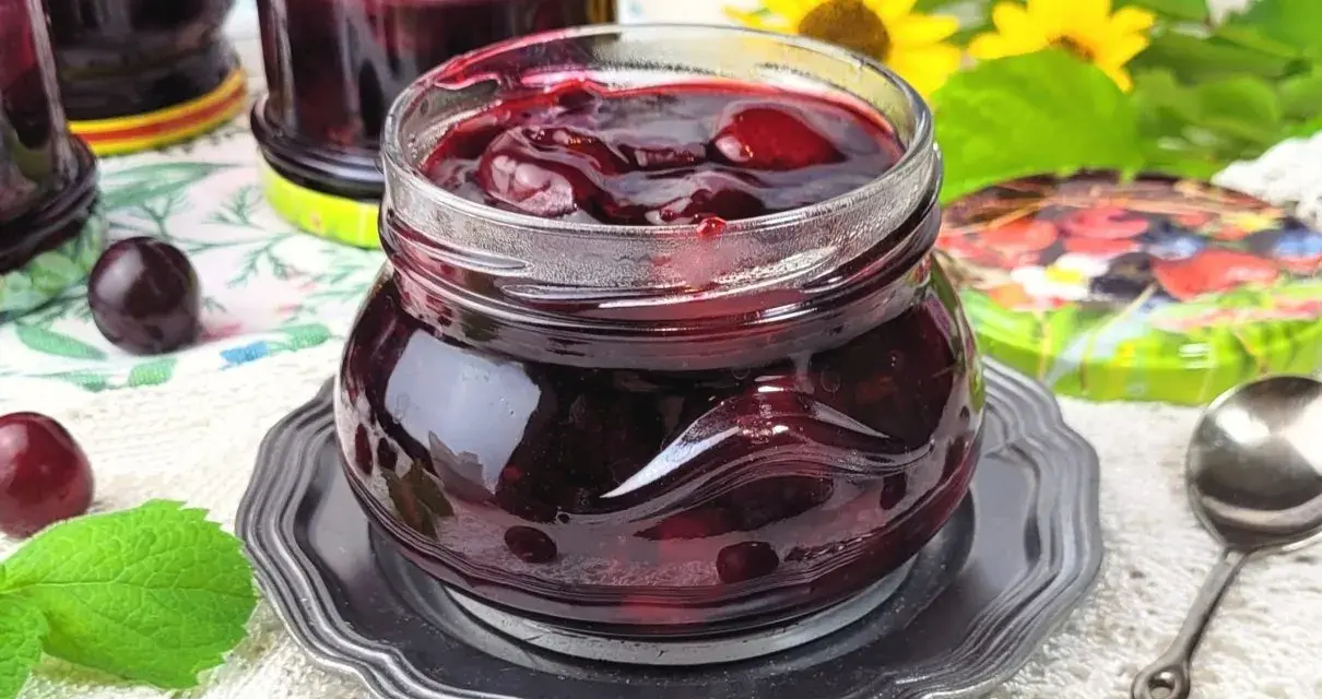 Słoiczek pełen wiśniowej frużeliny, obok świeże wiśnie i listki mięty.